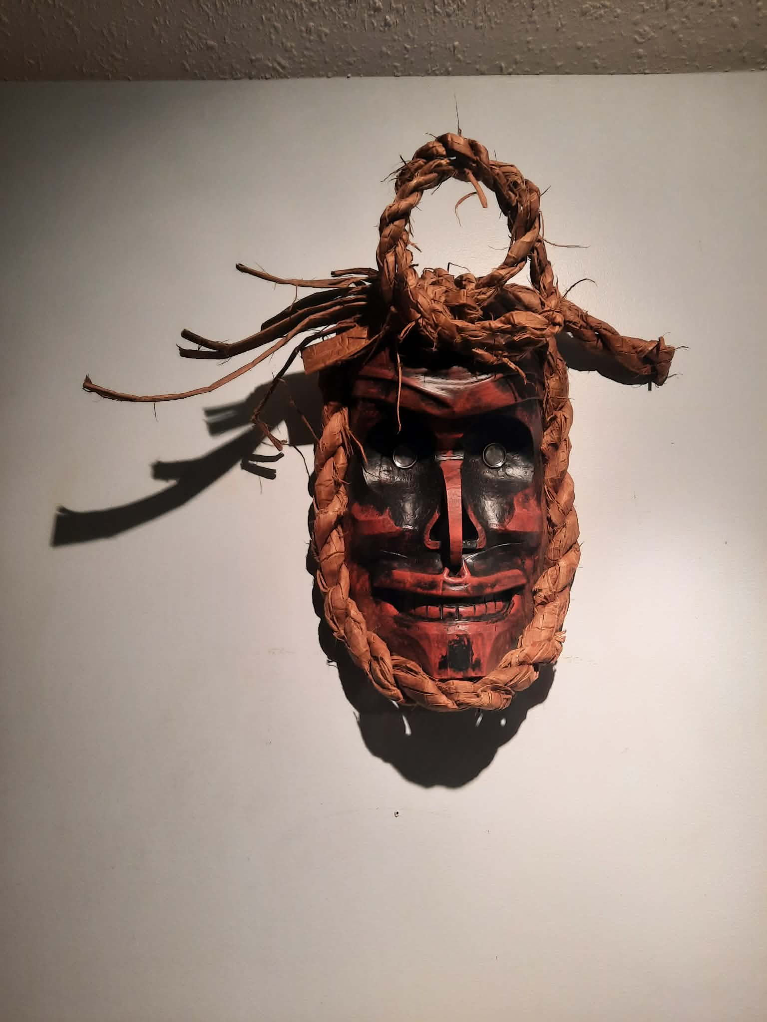 Red and black carved mask with cedar bark fringe
